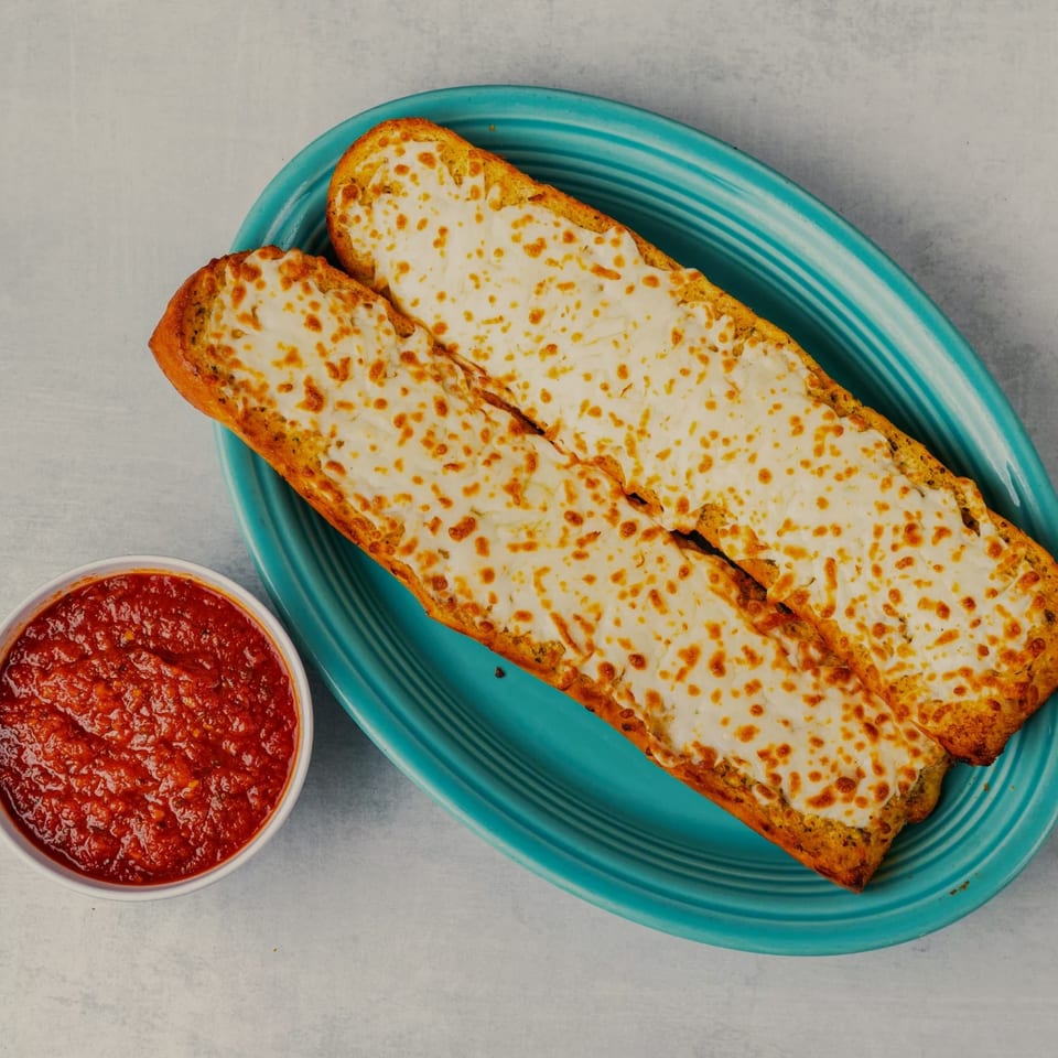 Two cheesy breadsticks on a blue plate with a side of marinara sauce.