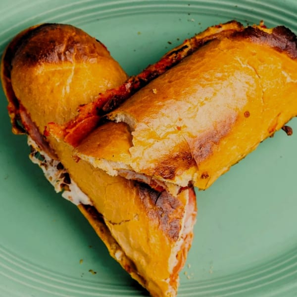 Two halves of a golden-brown calzone, filled with cheese and sauce, arranged in a heart shape on a green plate.