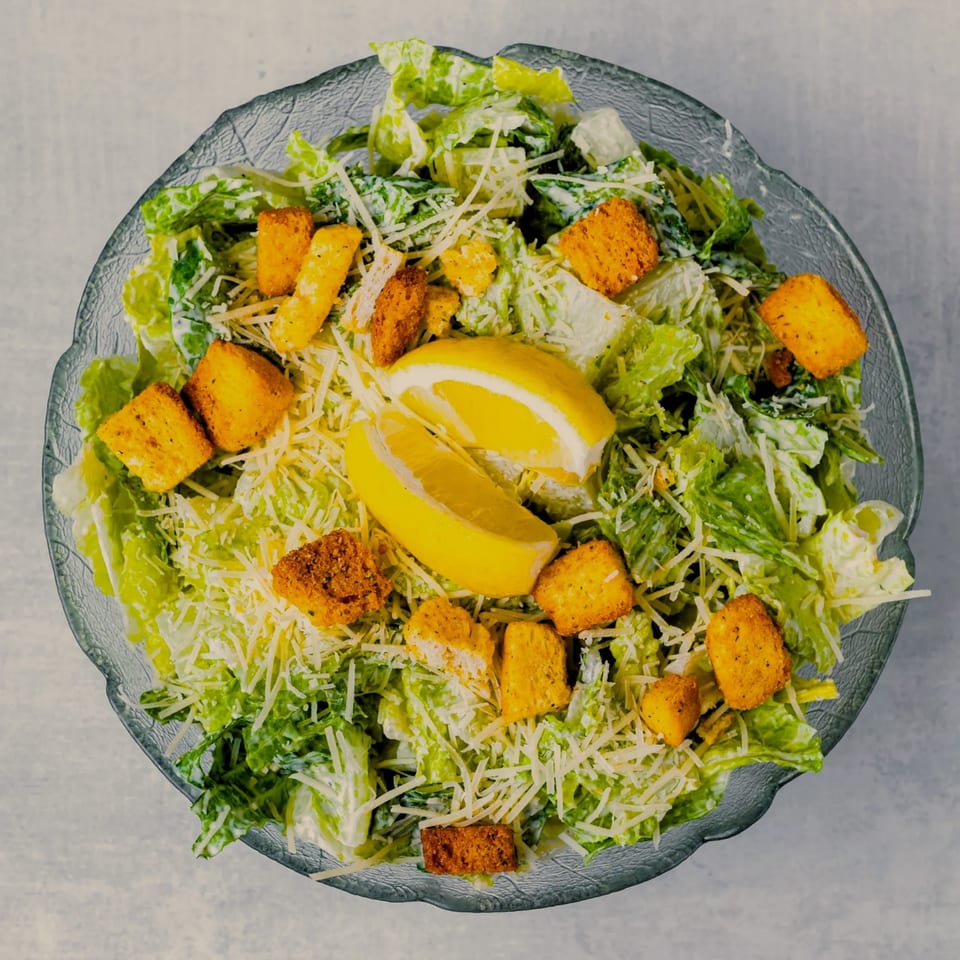 A Caesar salad with romaine lettuce, croutons, shredded Parmesan cheese, and lemon wedges.