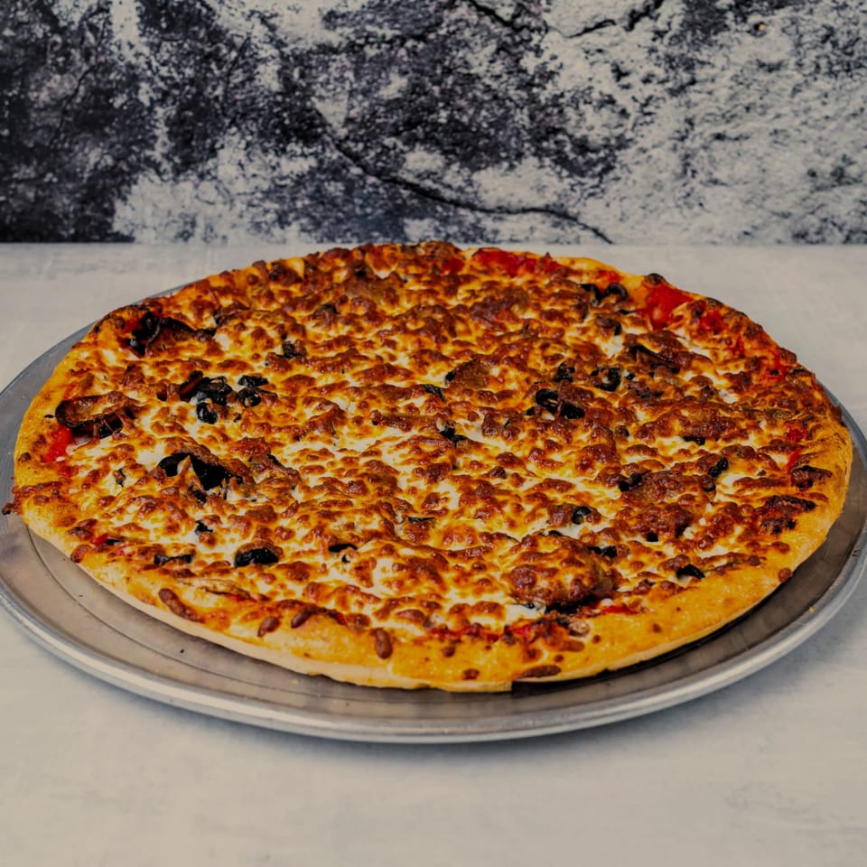 A whole SilverLake Pizza & Pasta pizza with melted cheese, black olives, and red peppers on a metal tray.
