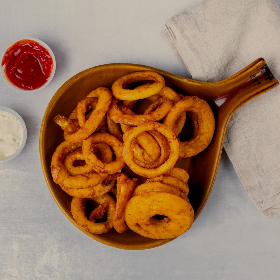 A brown bowl of crispy golden onion rings, with ketchup and ranch dressing on the side.