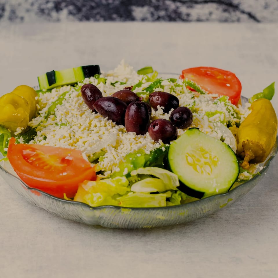 A fresh Greek salad with lettuce, tomatoes, cucumbers, olives, pepperoncini, and feta cheese.