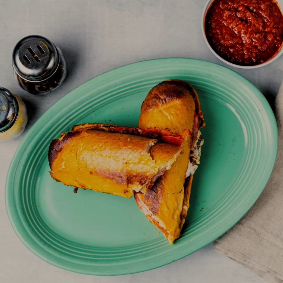 A SilverLake Pizza & Pasta calzone, cut in half, on a green plate with marinara and shakers.